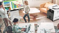 Four people in an office at desks and using an interactive display