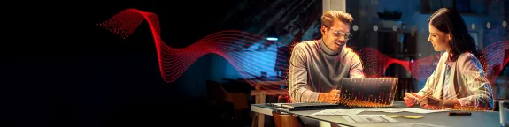 Man and a Woman sat a table, both looking at a laptop whilst talking 